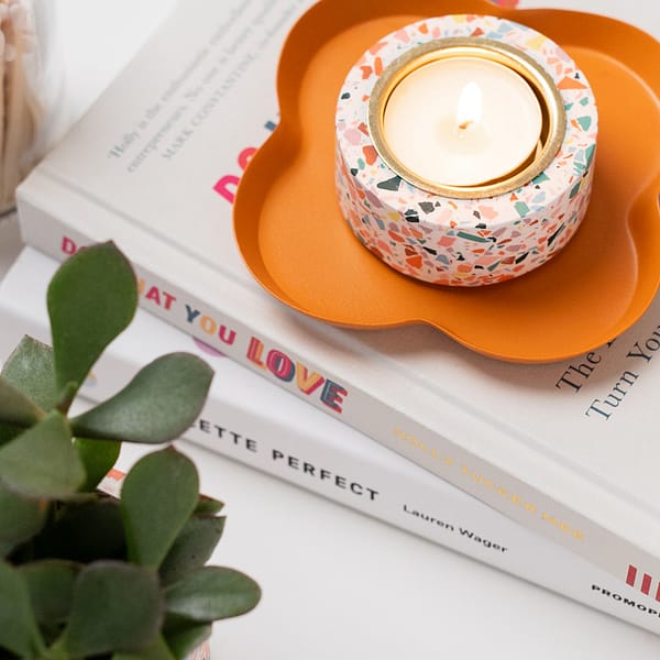 Single tealight holder with a tealight inside sitting a trinket tray. The tealight holder has a white based with coloured terrazzo patterning.