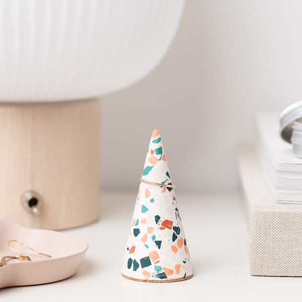 Handmade white ring tree with neutral mosaic pattern on bedside table. Styled next to a stack of books, table lamp and decorative tray.